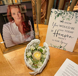 A memorial table features a framed photo of a woman, a sign reading We know you would be here today if heaven wasn't so far away, and a candle with angel wings.