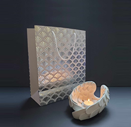 A decorative gift bag with an intricate pattern stands next to an elegant candle holder shaped like a swan, casting a warm, soft glow.