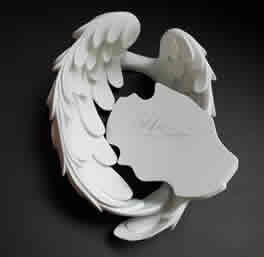 A white, sculptural piece resembling a stylized swan with flowing, curved wings, resting on a dark background. It conveys elegance and grace.